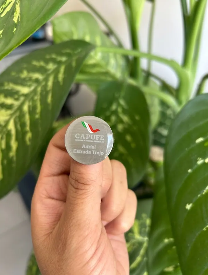Pin redondo con logotipo y nombre, sostenido en la mano