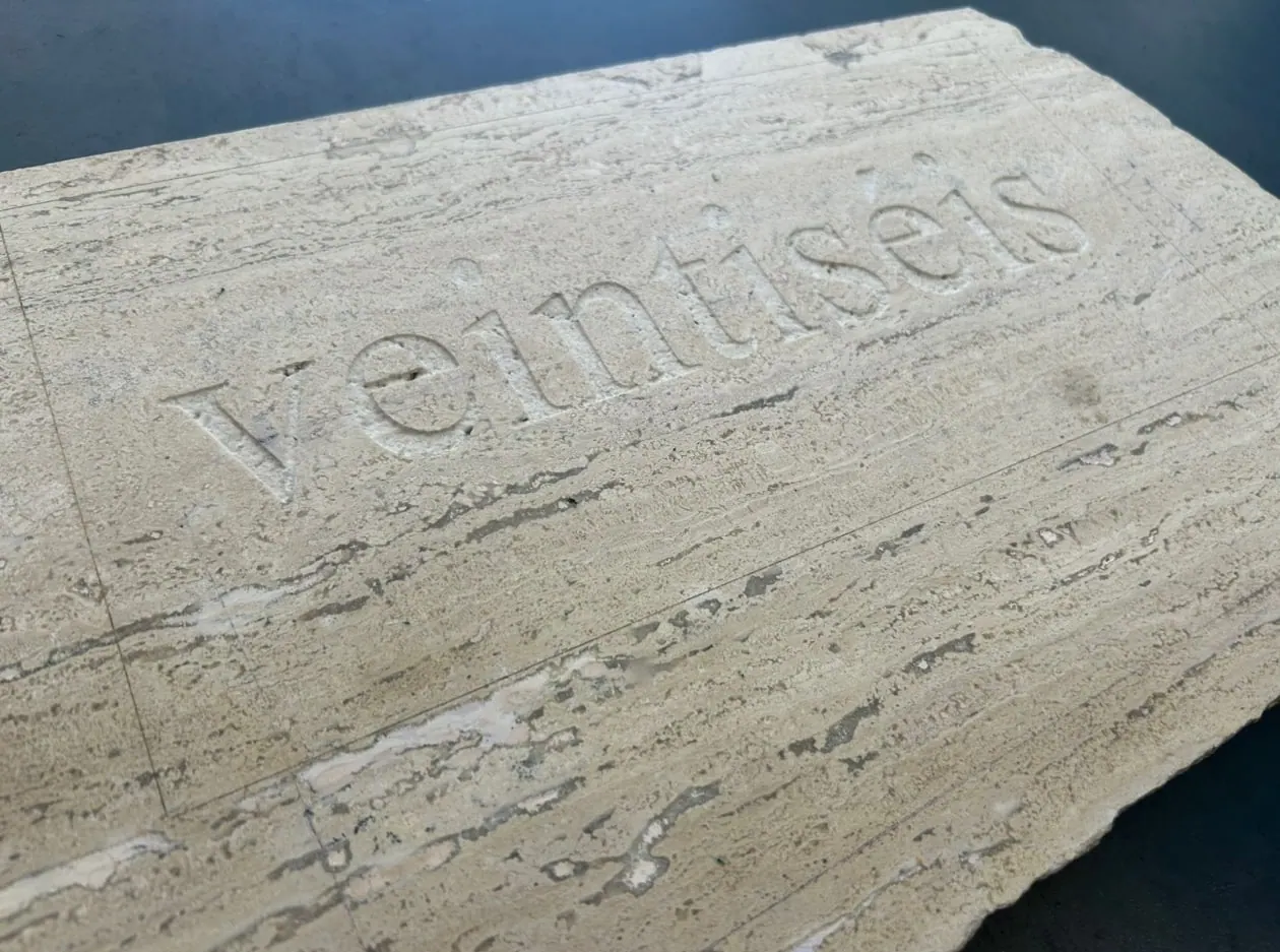 La palabra veintiséis grabada en bajorrelieve sobre una losa de travertino